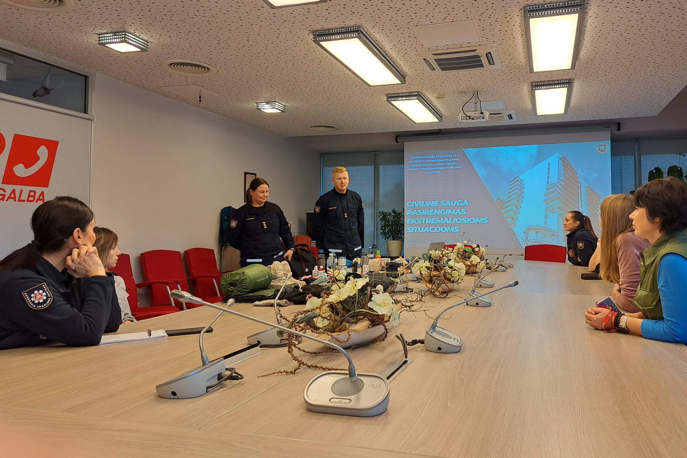 Nuotraukoje matomi du lektoriai ir aplink stalą susėdę Bendrojo pagalbos centro darbuotojai