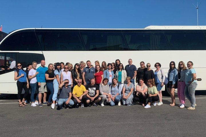 Nuotraukoje matoma didelė grupė darbuotojų prie autobuso