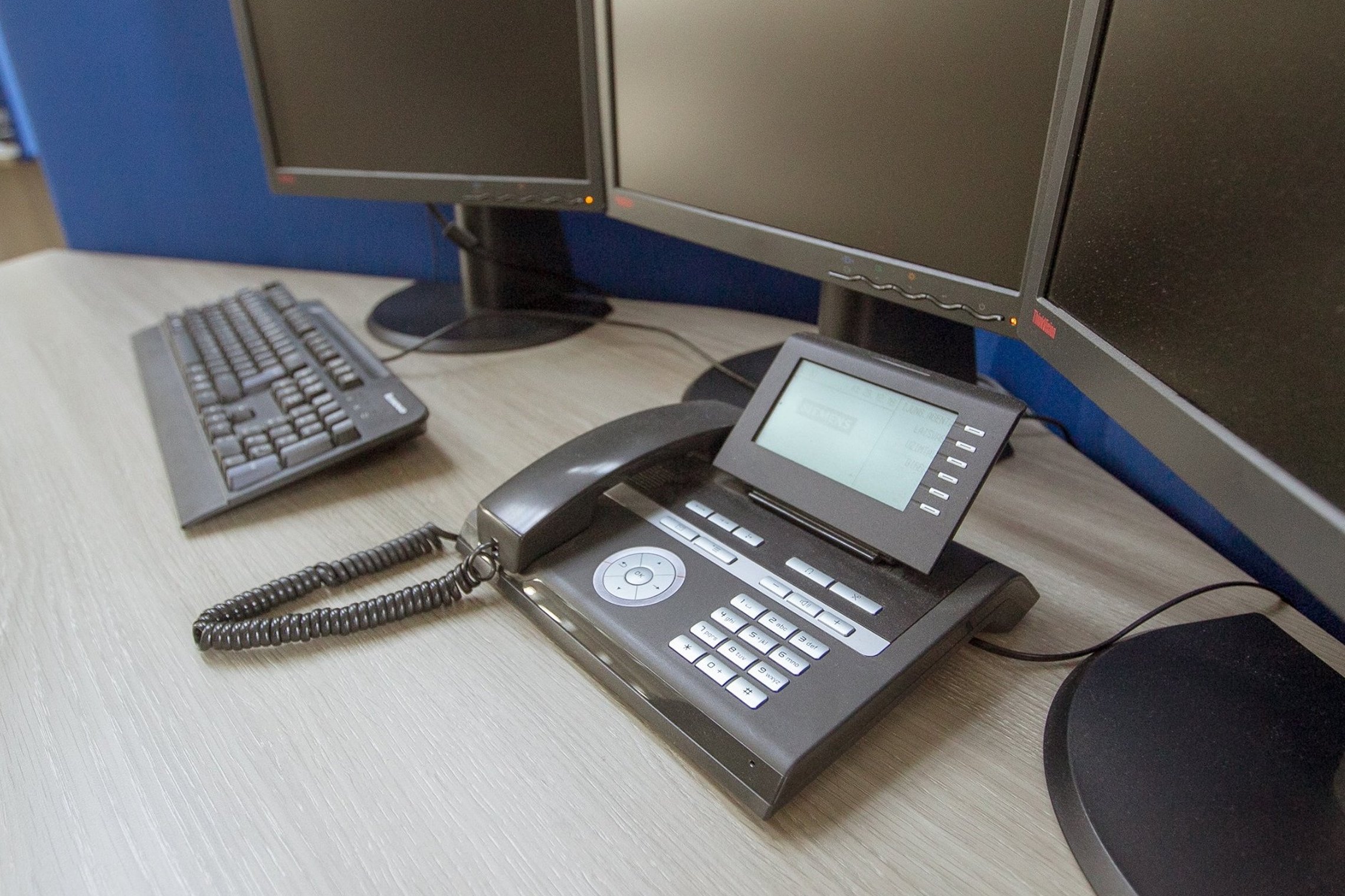 Nuotraukoje matomas operatorių telefonas, klaviatūra ir monitoriai