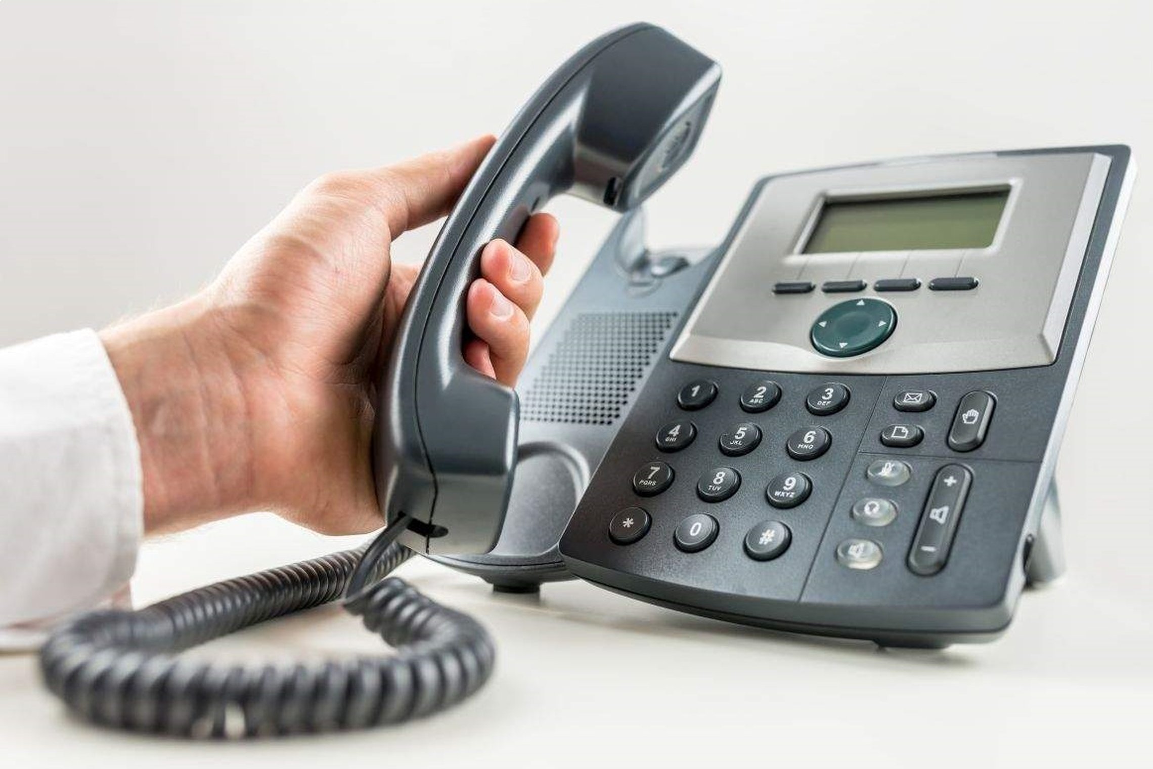 Nuotraukoje matomas telefono aparatas ir rankoje laikomas nukeltas ragelis