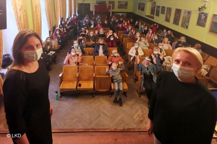 Nuotraukoje matomos dvi ant scenos stovinčios moterys ir salė su klausytojais