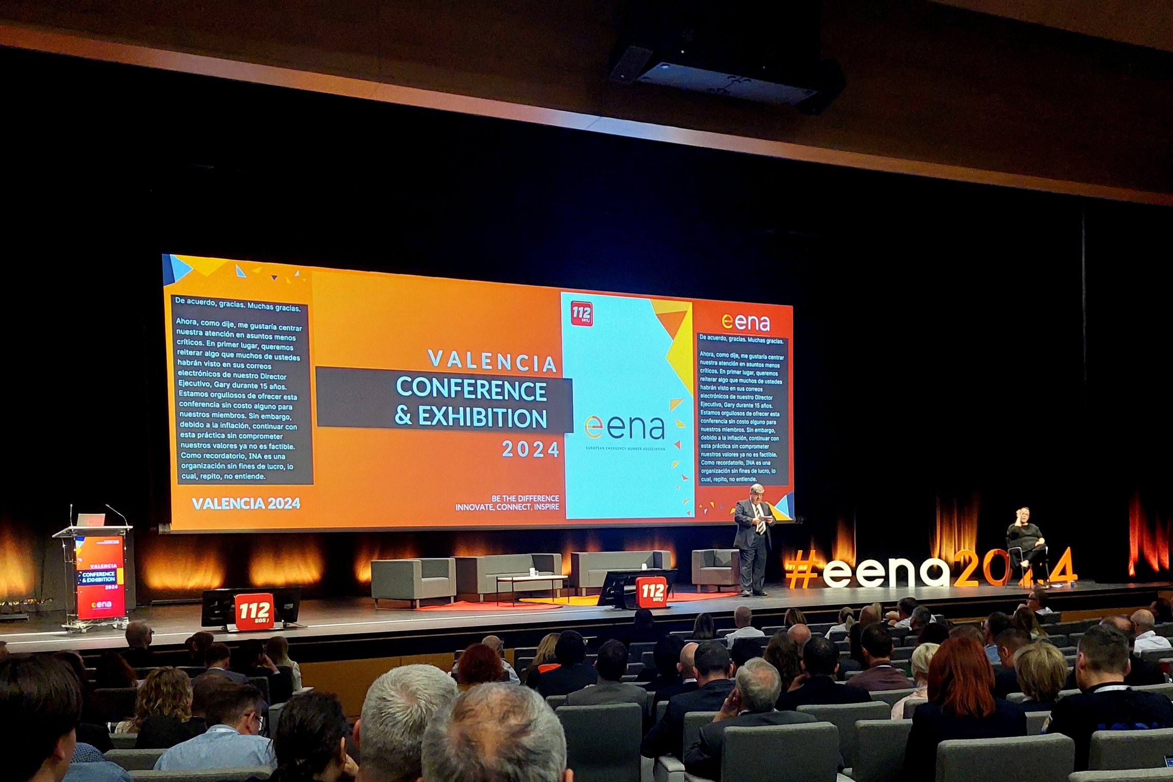 Nuotraukoje matoma didelės salės scena ir ekranas su konferencijos užsklanda anglų kalba