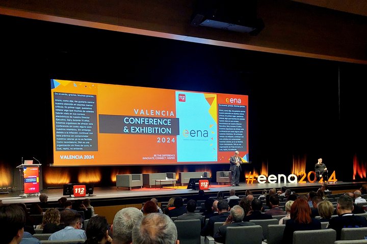 Nuotraukoje matoma didelės salės scena ir ekranas su konferencijos užsklanda anglų kalba