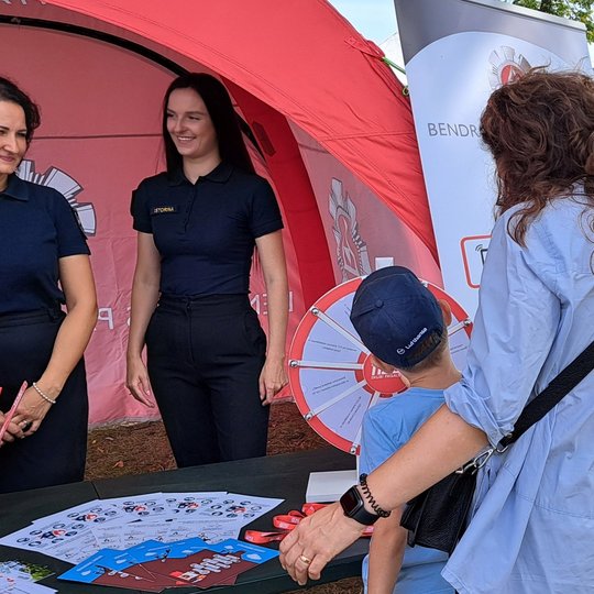 Nuotraukoje matomos palapinėje stovinčios Bendrojo pagalbos centro darbuotojos ir prie jų priėjęs vaikas su mama