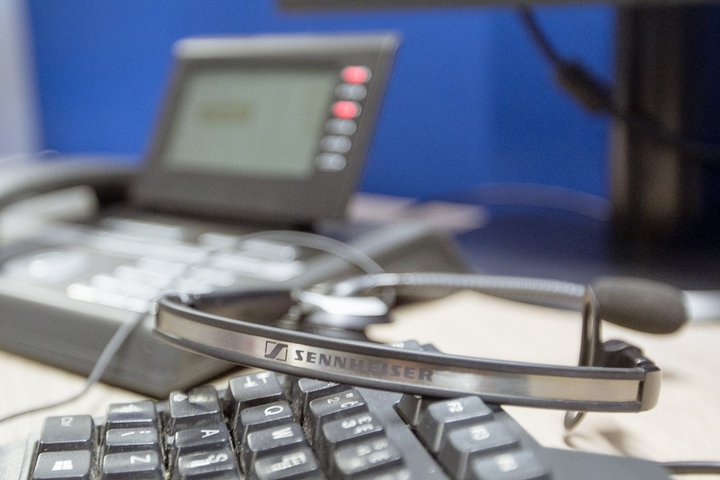 Nuotraukoje matomas operatoriaus telefonas, kompiuterio klaviatūra ir ausinės