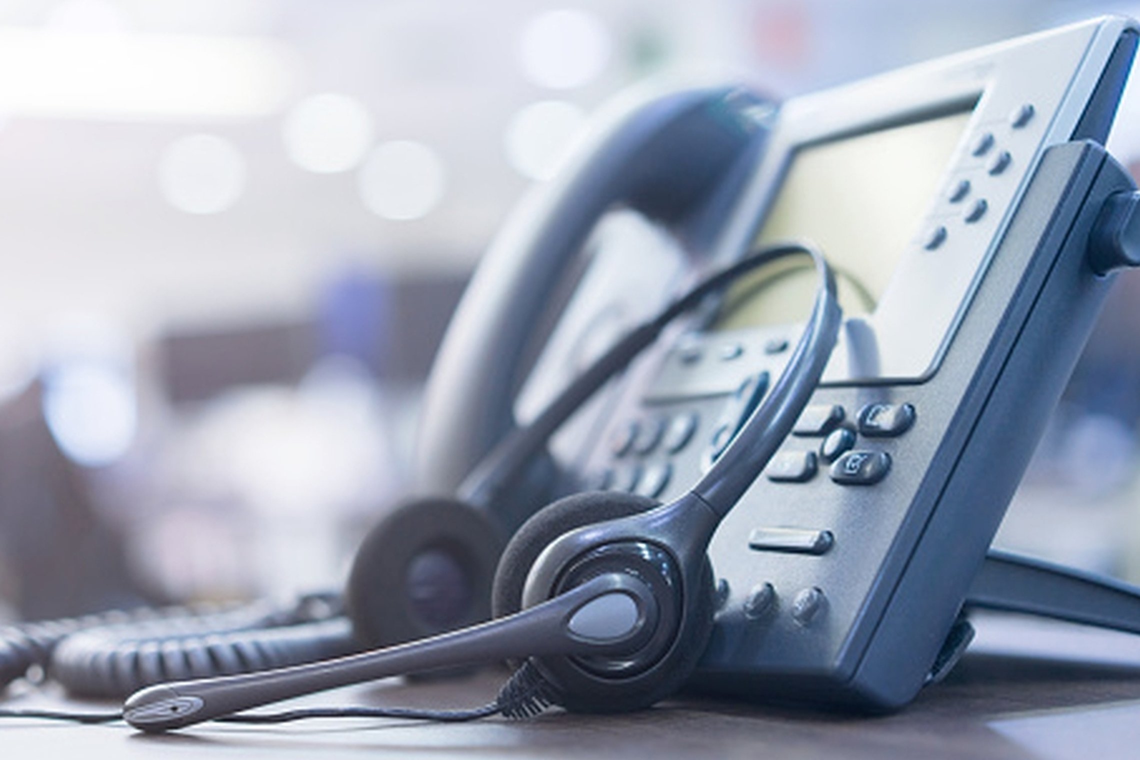 Nuotraukoje matomas ant stalo stovintis stacionarus telefonas ir į jį atremtos ausinės
