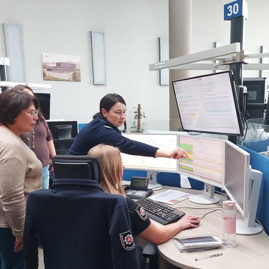 Nuotraukoje matoma Vilniaus skyriaus viršininkė rodanti viešnioms kažką operatoriaus monitoriuje