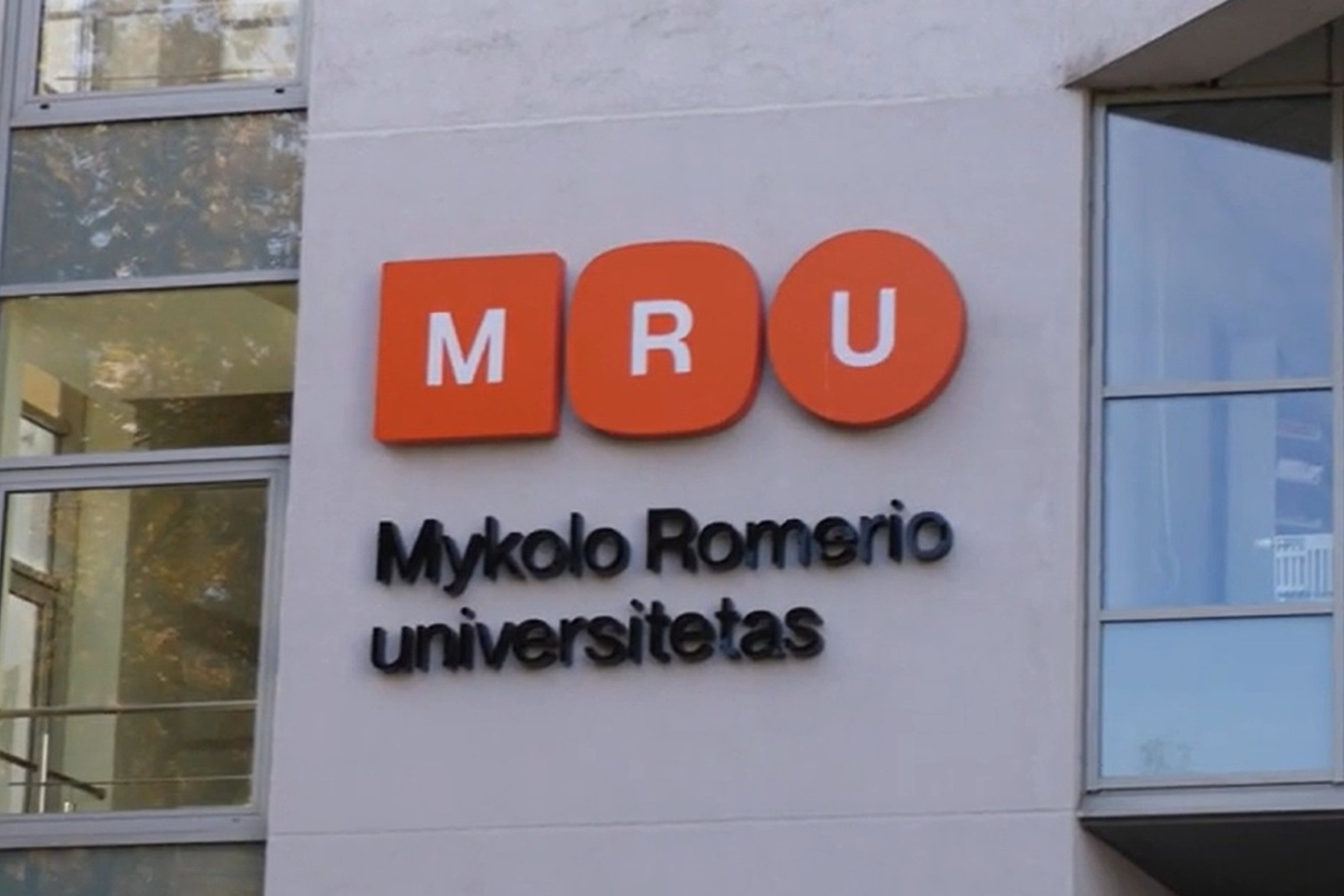 Nuotraukoje matomas pastato fasado fragmentas su universiteto pavadinimu ir logotipu