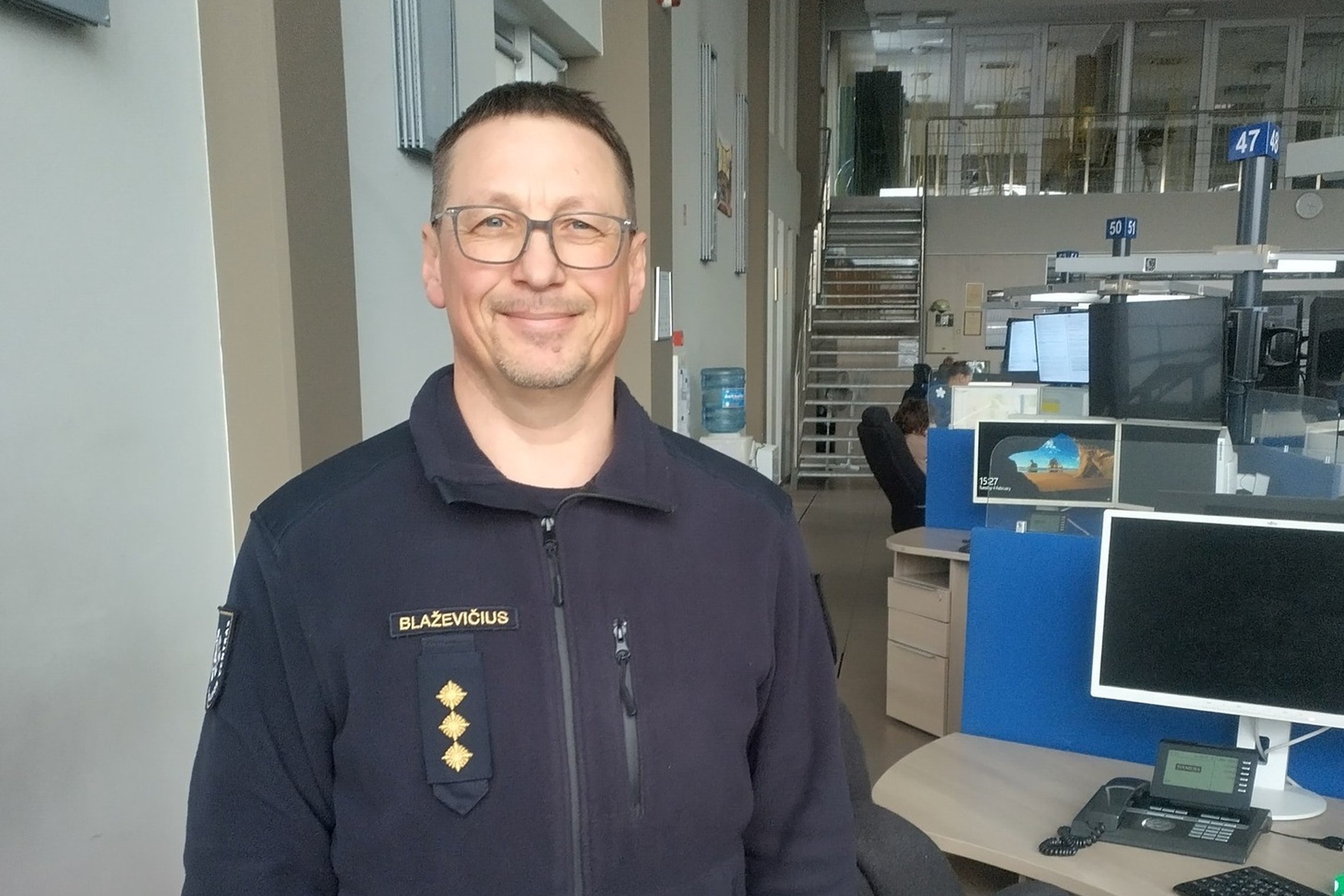 Nuotraukoje iki krūtinės matosi operatorių salėje stovintis ir besišypsantis pareigūnas