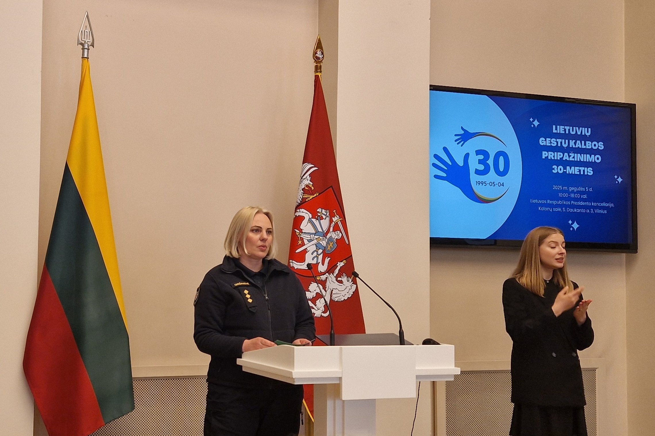 Nuotraukoje matoma prie pranešėjo tribūnos stovinti pareigūnė ir jai iš kairės – gestų kalbos vertėja